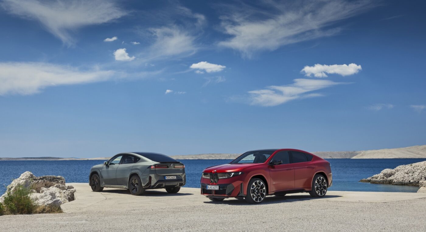 Dve verzie nového BMW iX4 na pobrežnej ceste, červená a sivá.