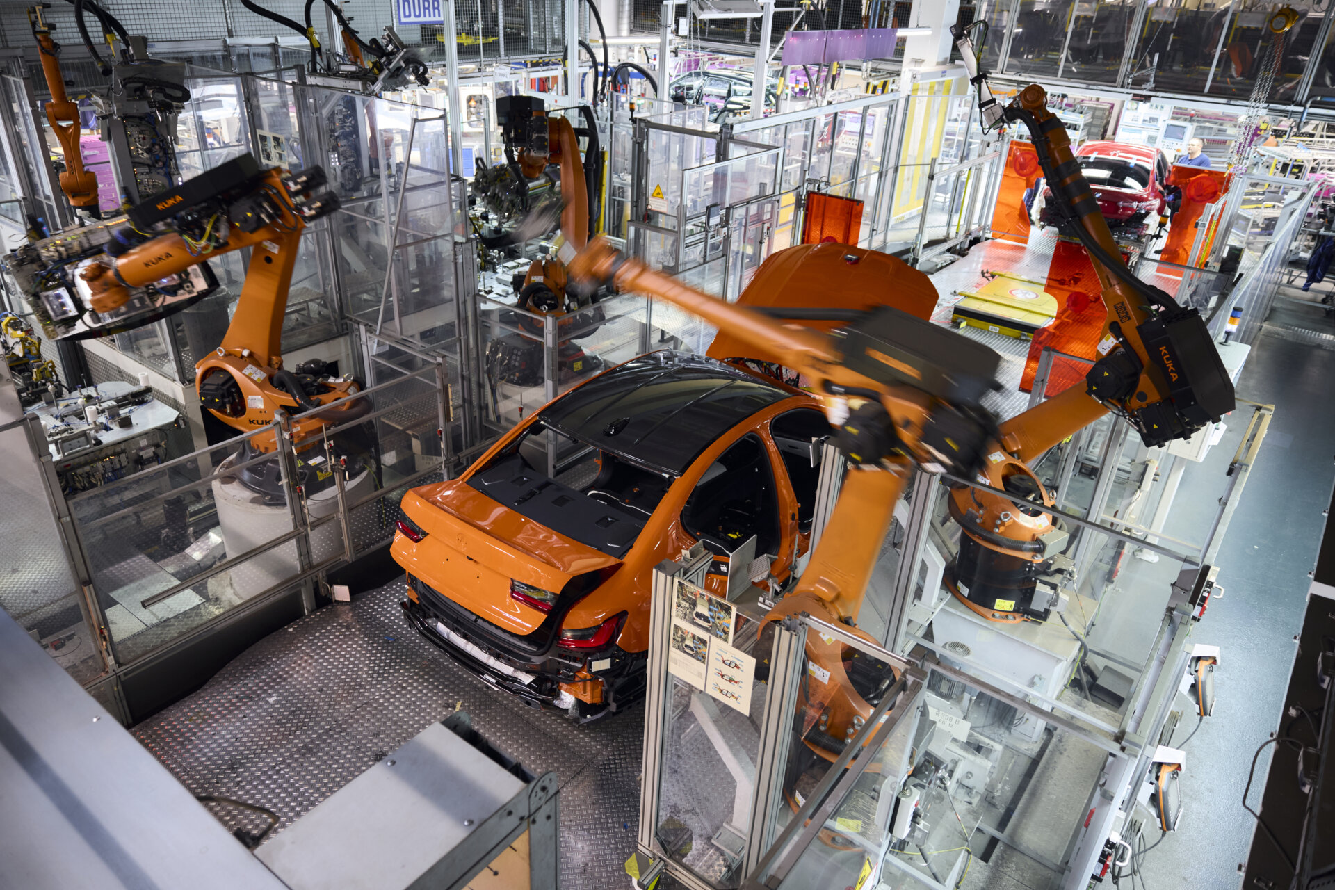 Oranžové BMW M3 vo výrobnom procese medzi robotmi mníchovskej fabriky.